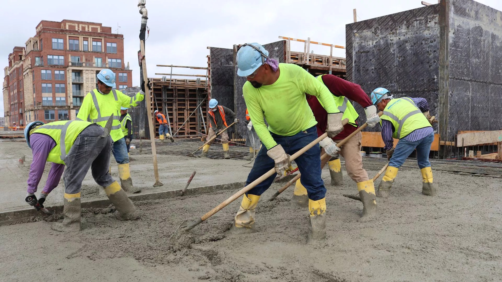 Construction workers in hard hats leveling out cement on a building